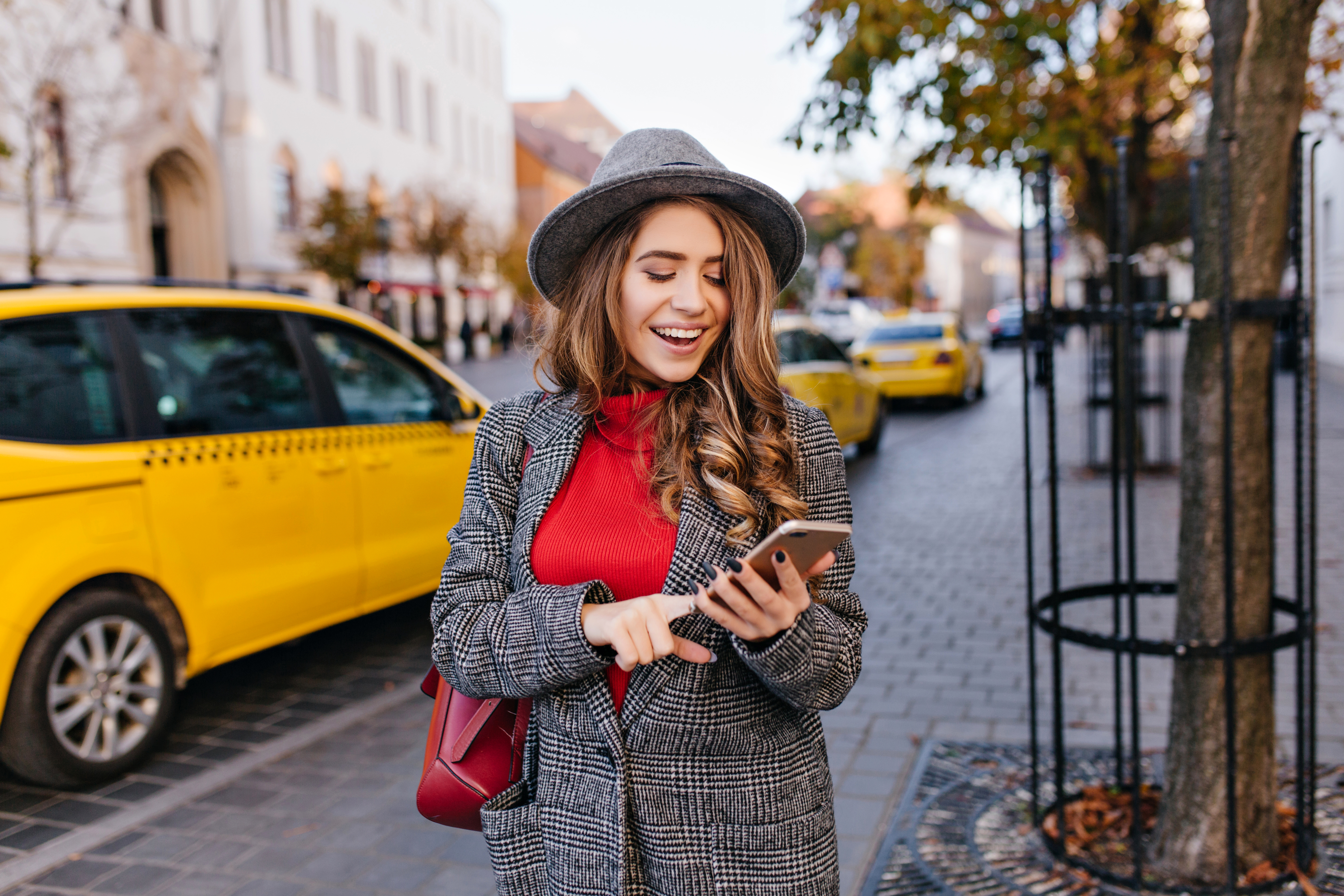 Good looking business woman texting message while walking on the street. Refined lady in elegant coat looking at phone screen, standing on avenue with taxi on background..